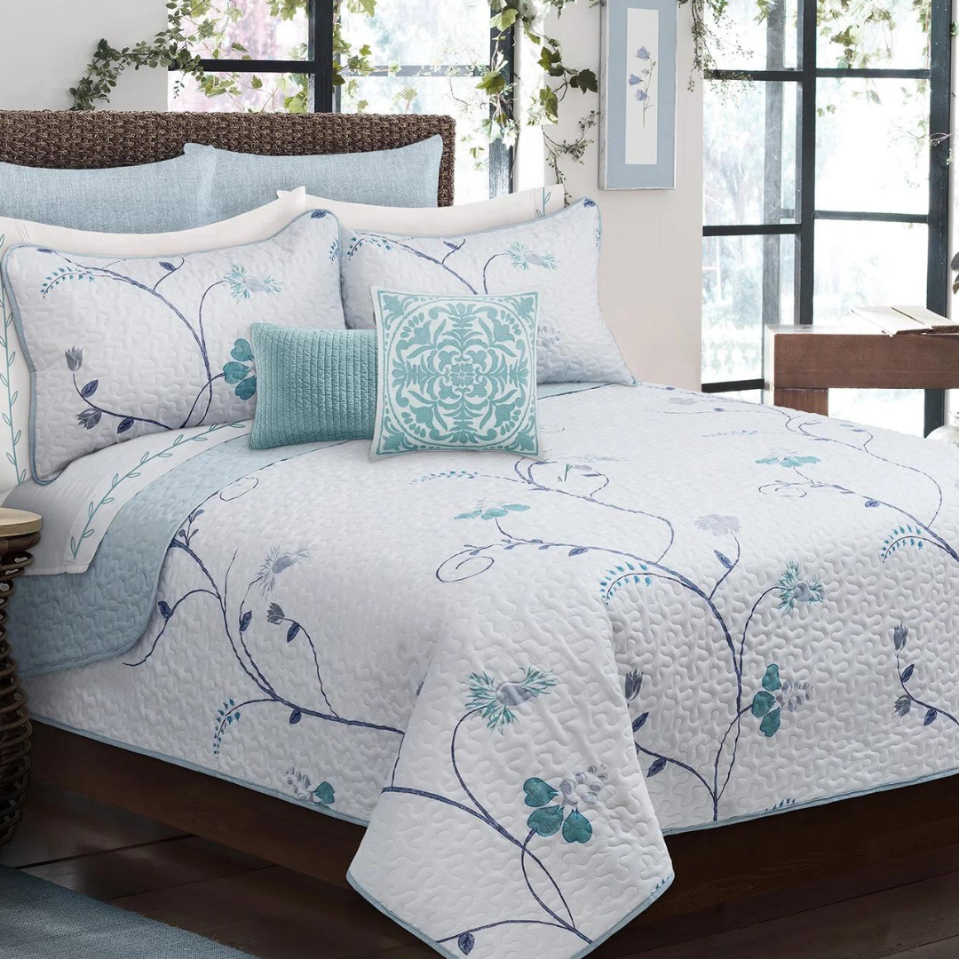 A bed with floral-patterned bedding including quilt, pillows, and decorative cushions in blue and white colors.
