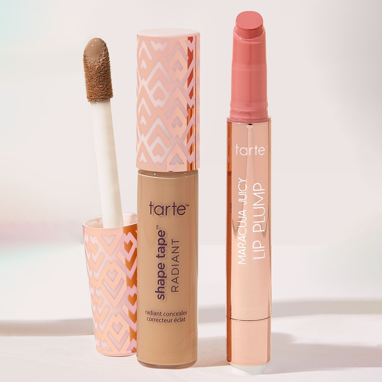 Tarte Shape Tape & Lip Color Set features a radiant concealer with a large applicator and a Maracuja Juicy Lip Plump in a sleek, twist-up tube, both with a pink and white geometric design on the packaging.