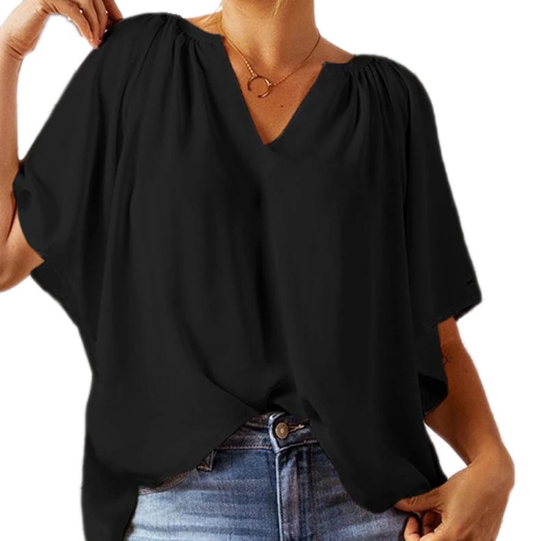 Black oversized V-neck top with short sleeves and gathered detail at the shoulders, tucked into light blue jeans.