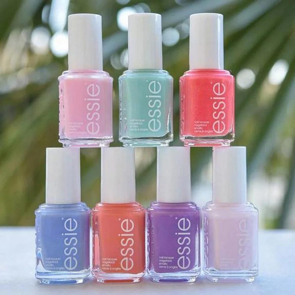 Six bottles of Essie nail polish in various shades of pink, purple, blue, and red.