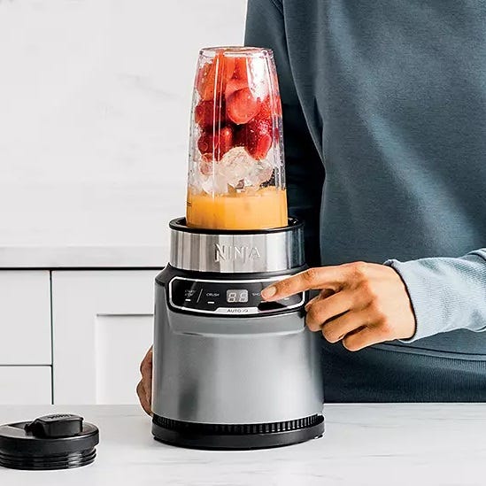 A Ninja blender with sliced fruits is being operated by a person.