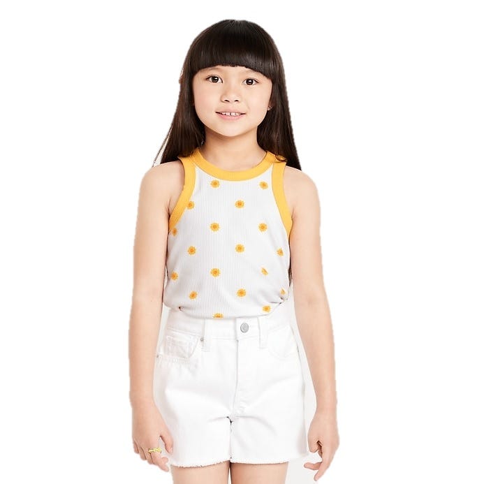 A girl is wearing a sleeveless tank top with yellow borders and small yellow flower prints, paired with white shorts.