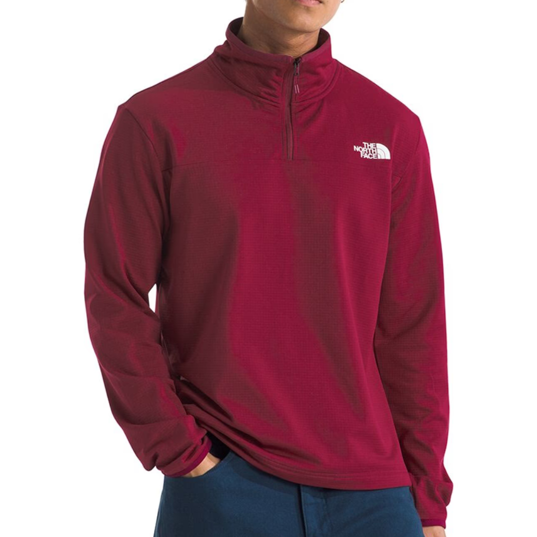 A male model is wearing a maroon The North Face quarter-zip pullover paired with blue pants.