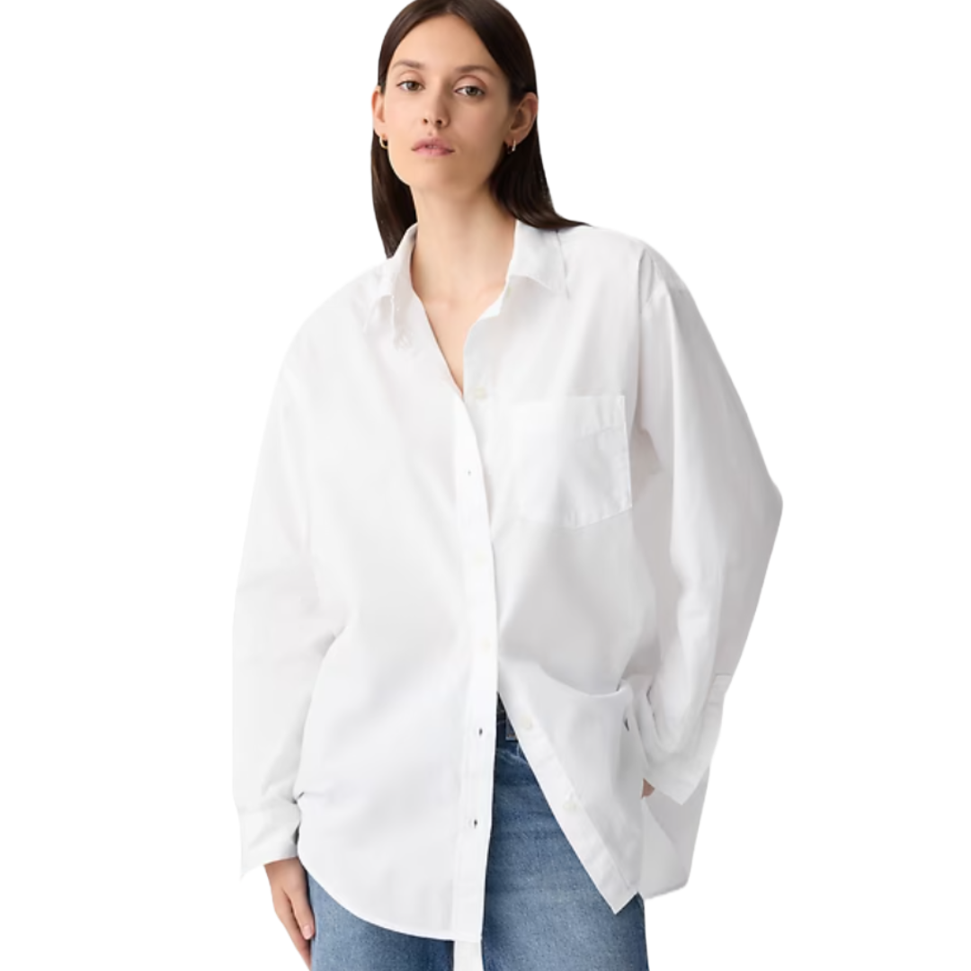 A woman in a white, oversized button-up shirt with a front pocket and blue jeans.