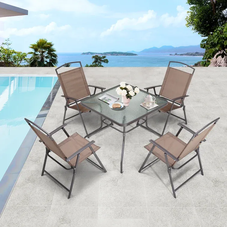 Outdoor patio furniture set with a glass-top table and four folding chairs on a poolside terrace.