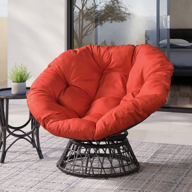 A red papasan chair with a black base and a small round side table with a green plant.