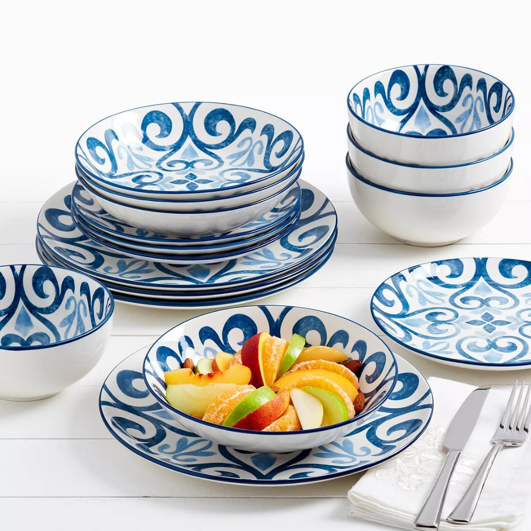 A set of blue and white patterned dinnerware including plates, bowls, and a fruit-filled dish with silverware on the side.