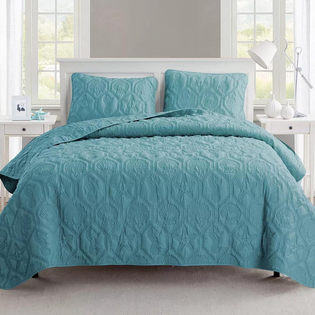 A teal quilted comforter set on a bed, with matching pillow shams.