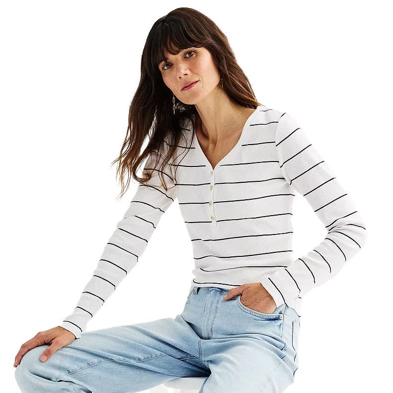 A woman is wearing a white, long-sleeve, V-neck top with black stripes, paired with light blue jeans.