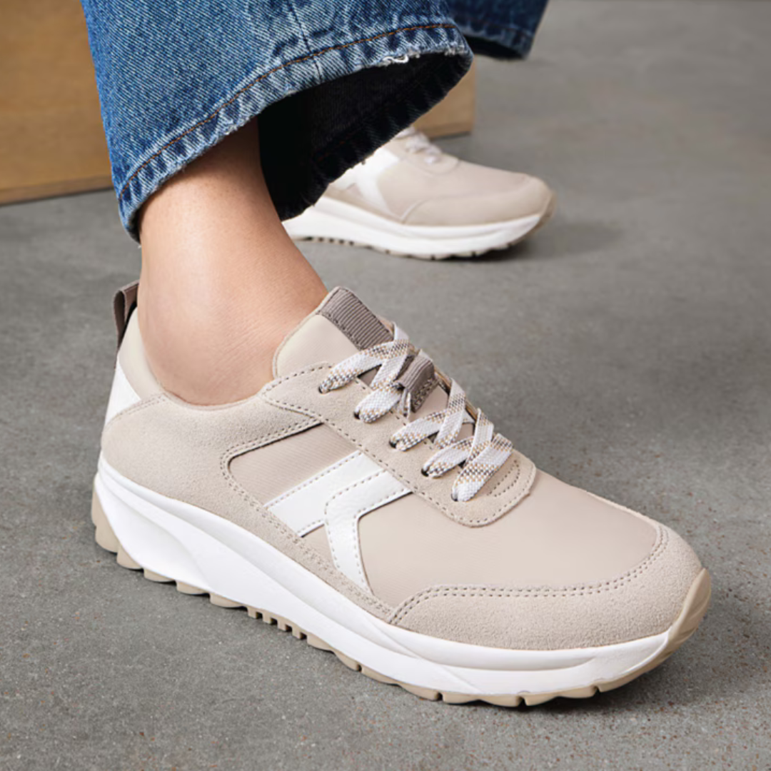 Stylish beige sneaker with white detailing and a thick sole. The shoe is paired with blue jeans, showcasing a casual, modern look.