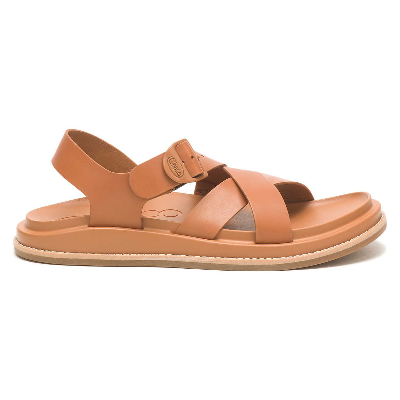 A tan sandal with a strap over the ankle and a crisscross design over the foot, featuring a buckle and a flat sole.