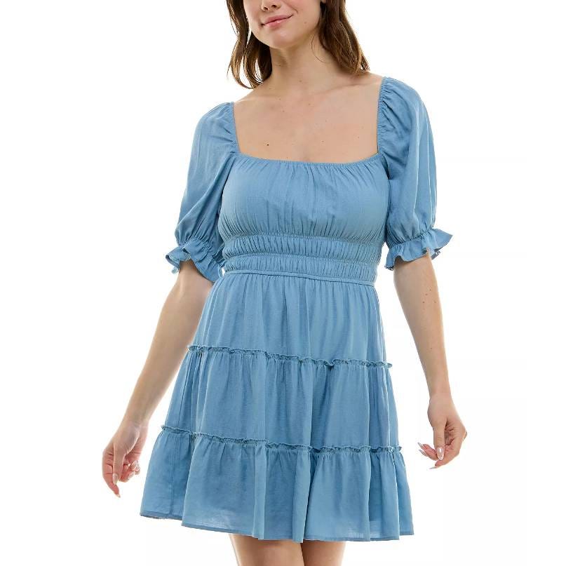 A woman wearing a blue, short-sleeved tiered dress with scoop neckline and ruffle details.
