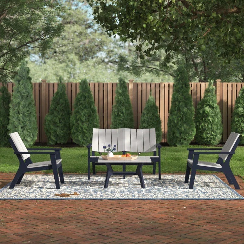 Outdoor patio set with a bench, two chairs, and a coffee table, on a patterned rug.