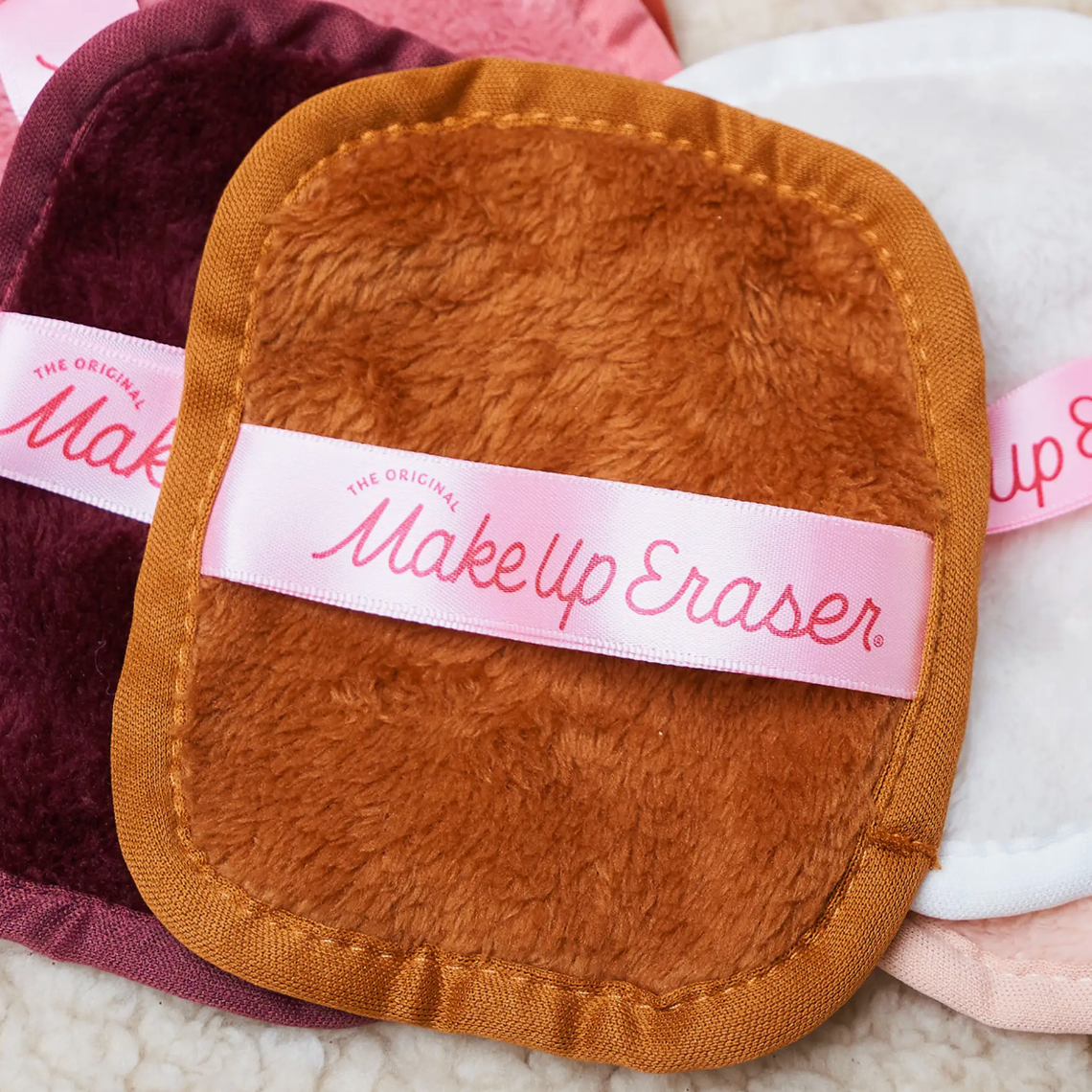 Soft, colorful Makeup Eraser cloths featuring a pink ribbon with the brand's name are visible. They're designed for removing makeup.
