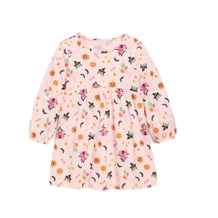 A pink children's dress featuring a Halloween theme with illustrations of witches, pumpkins, bats, and stars. The dress has long sleeves and a gathered waistline.