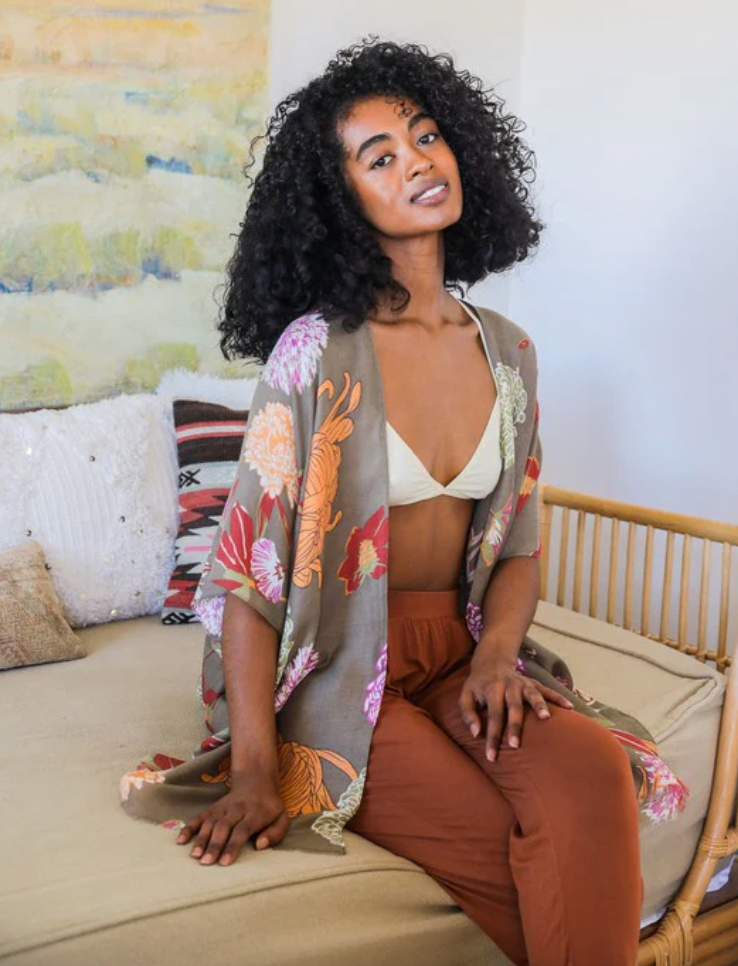 A woman wearing a floral kimono over a beige crop top paired with rust-colored trousers.