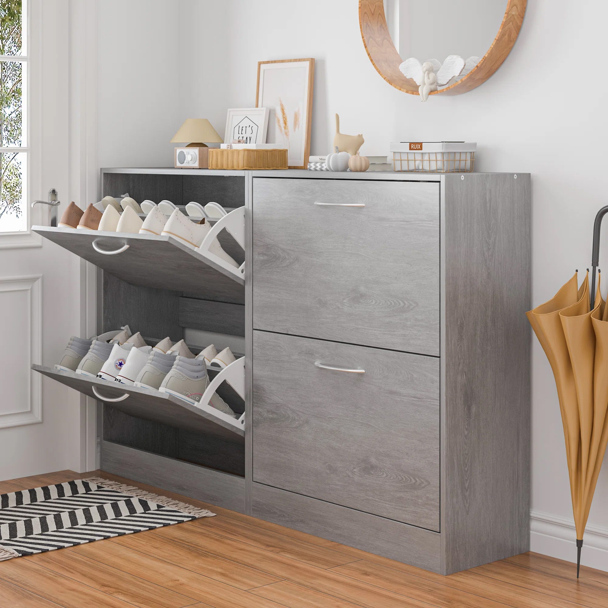 A grey shoe cabinet with pull-down drawers displaying various shoes and a decorative mirror and accessories on top.
