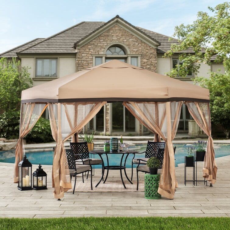 Hexagonal steel pop-up gazebo with a tan canopy and matching curtains tied back at the openings, set over patio furniture beside a pool.
