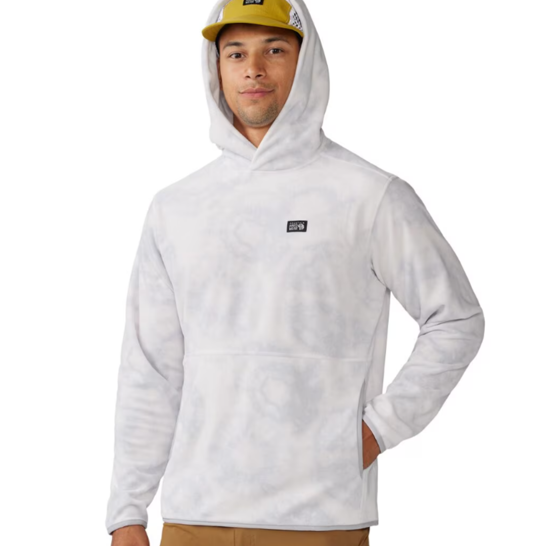 A person is wearing a white Mountain Hardwear Microchill hoodie with a front pouch pocket and brand logo on the chest, paired with a yellow cap and brown pants.