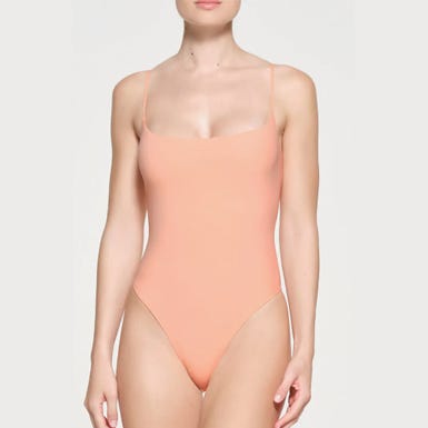 A person wearing a plain light orange one-piece swimsuit.