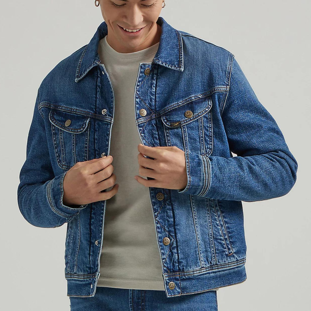 A man is wearing a blue denim jacket with a classic collar, button front, chest pockets, and a Sherpa lining that provides added warmth.