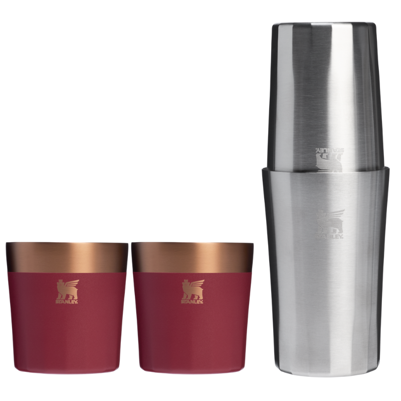Two red and copper tumblers are shown alongside a stainless steel cocktail shaker. Each tumbler features a logo with a winged lion.