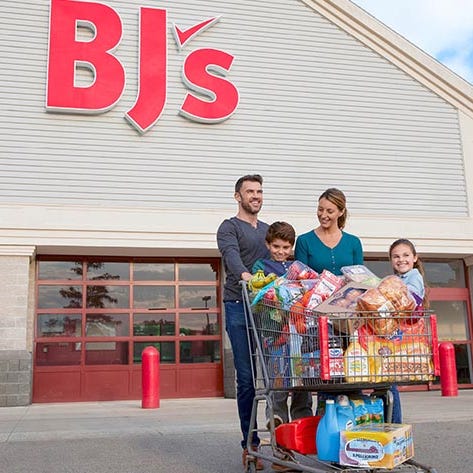 A family with a shopping cart filled with various grocery items outside a BJ's Wholesale Club.