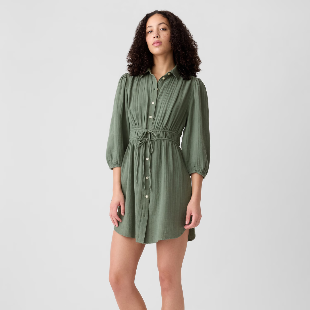 A woman is wearing a green, button-up dress with a drawstring waist and long sleeves.