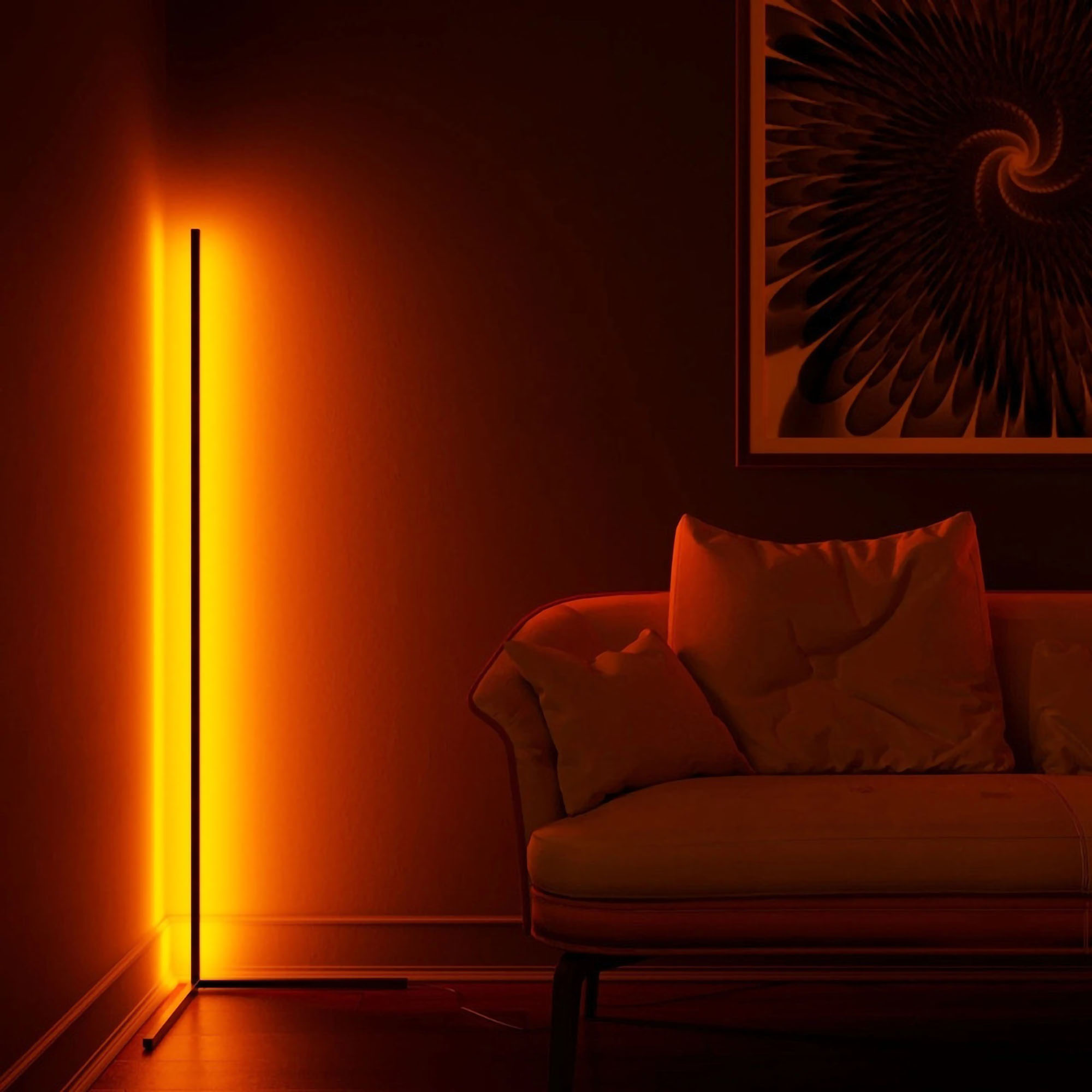 Vertical floor lamp casting an orange glow against the wall, next to a sofa with a cushion and a framed spiral artwork above.