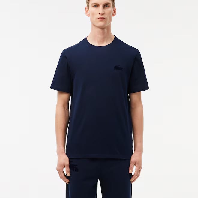 A man wears a dark blue Lacoste cotton t-shirt with a subtle, matching-color crocodile logo on the chest and short sleeves.