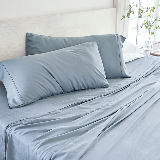 A neatly made bed with blue-gray bedding, including pillowcases, sheets, and a duvet cover.