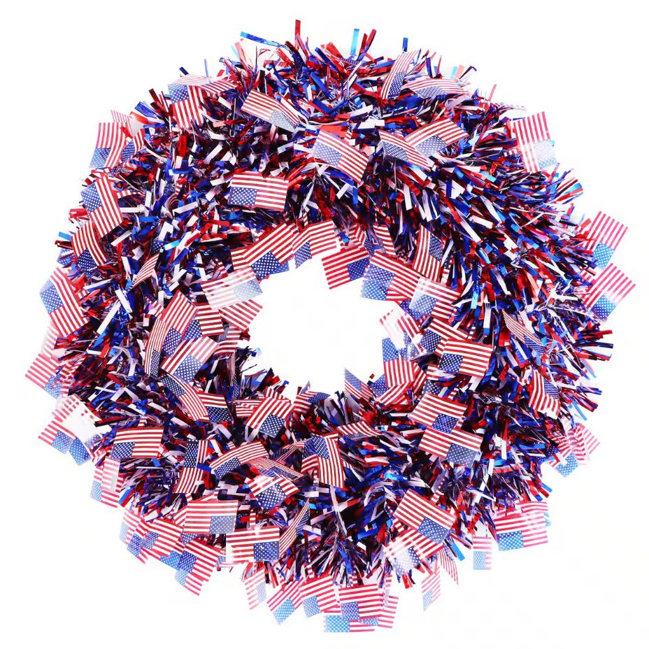 A circular wreath decorated with numerous small American flags and red, white, and blue tinsel.
