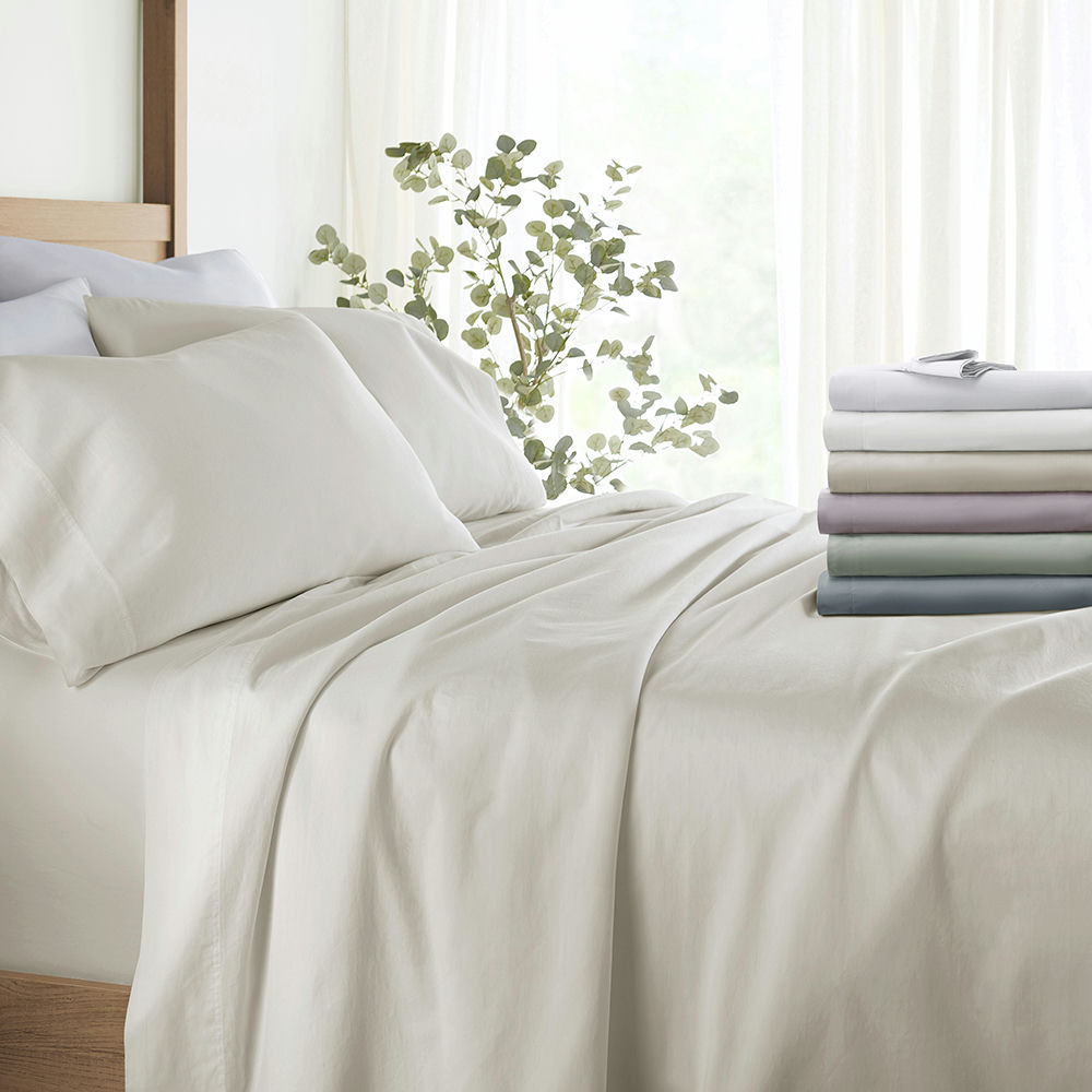 A neatly made bed with white bedding and a stack of folded sheets in various colors at the foot of the bed.