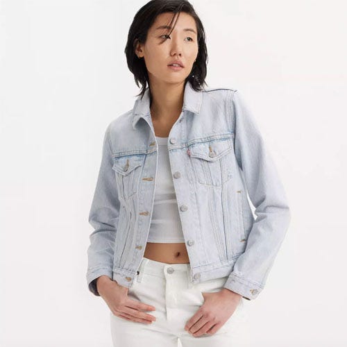 A woman wearing a light-wash denim jacket paired with white pants.