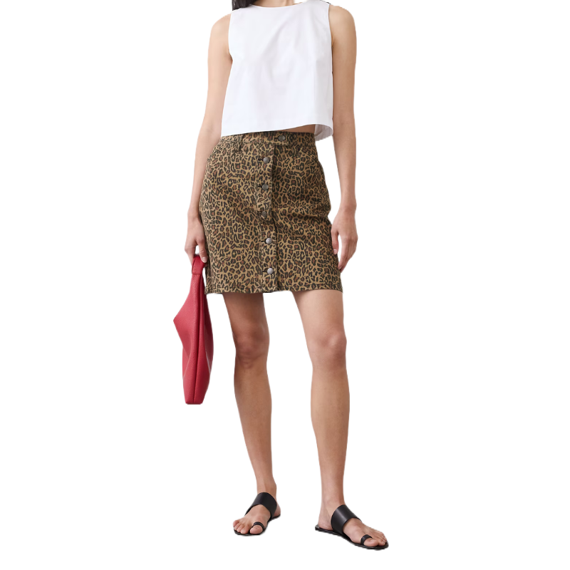 A person wears a white sleeveless top and a leopard print button-up skirt, paired with black sandals, holding a red handbag.
