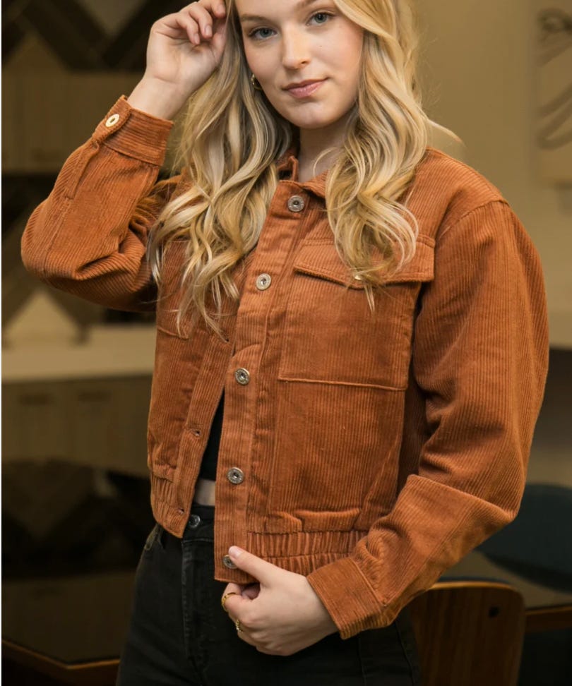 A woman is wearing a rust-colored corduroy jacket with front button closure and black pants.