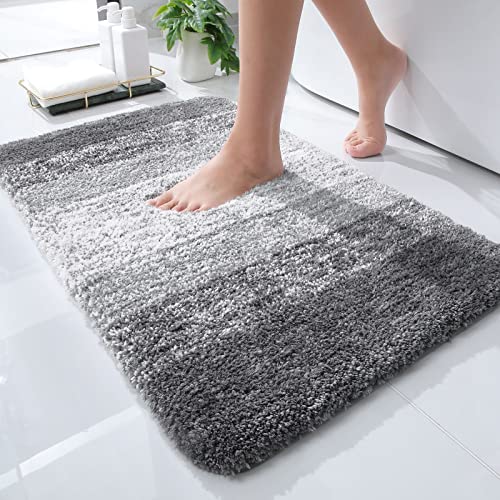 A plush, gradient gray bath rug with a person stepping on it, showcasing its soft texture on a glossy tiled bathroom floor.