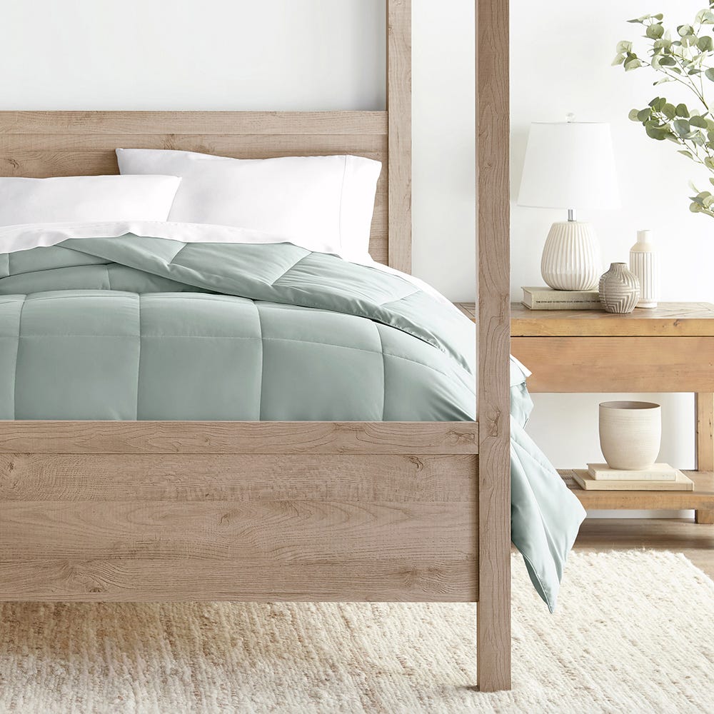 A wooden bed frame with a green comforter set, white pillows, bedside table, lamp, and decorative vases.