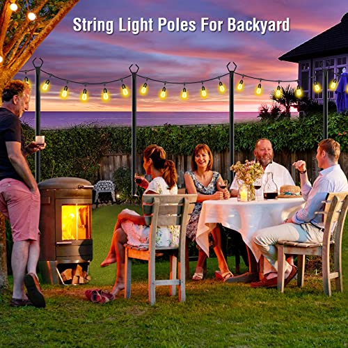 A set of poles designed to hold string lights over a backyard patio where people are gathered around a dining table and a firepit.