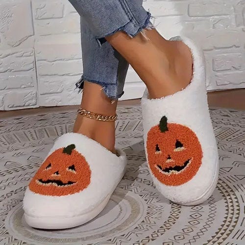 White slippers with orange pumpkin faces embroidered on the top.