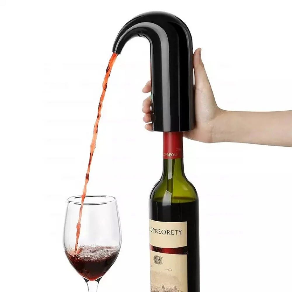 A hand is holding a black wine aerator over a glass, pouring red wine from a bottle through it.