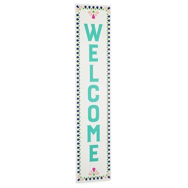 Vertical \“WELCOME\“ sign with teal letters, bordered with a pattern of blue and pink accents.