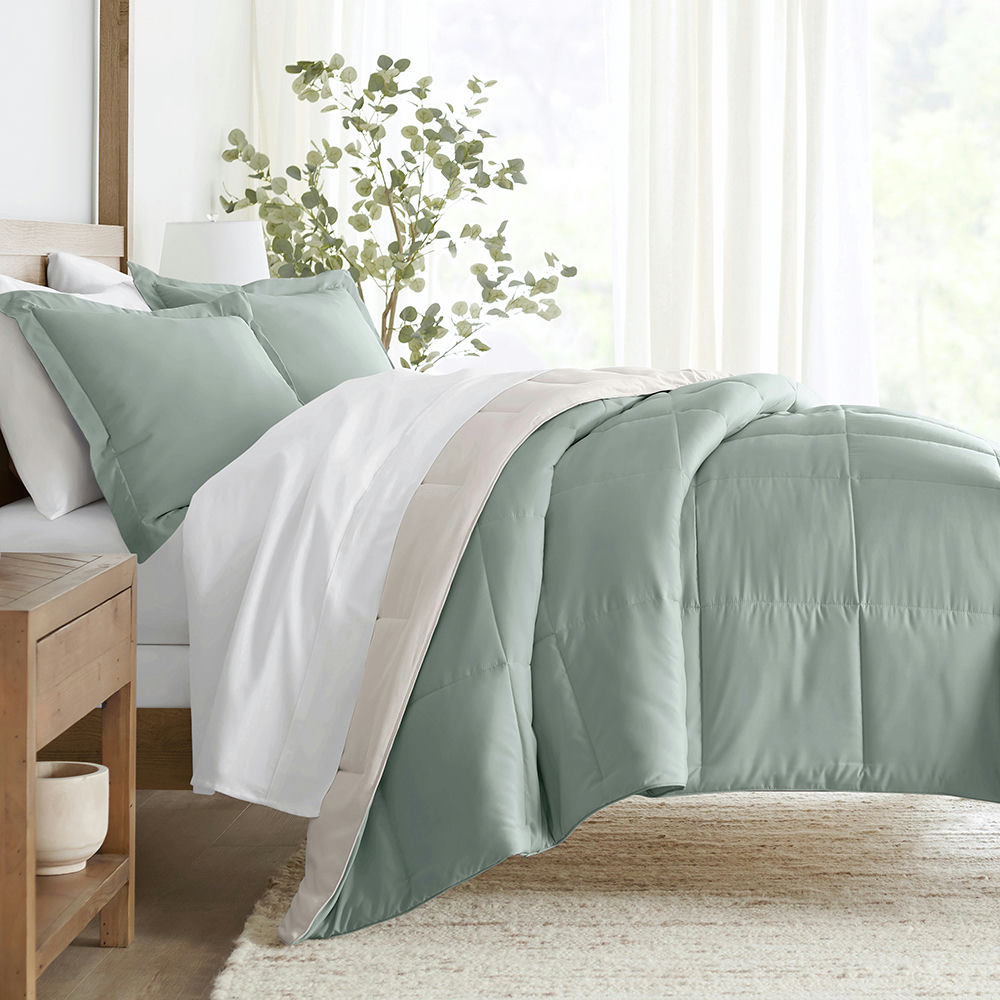 Bed with green duvet cover, white sheets, and complementary pillows in a bright room.