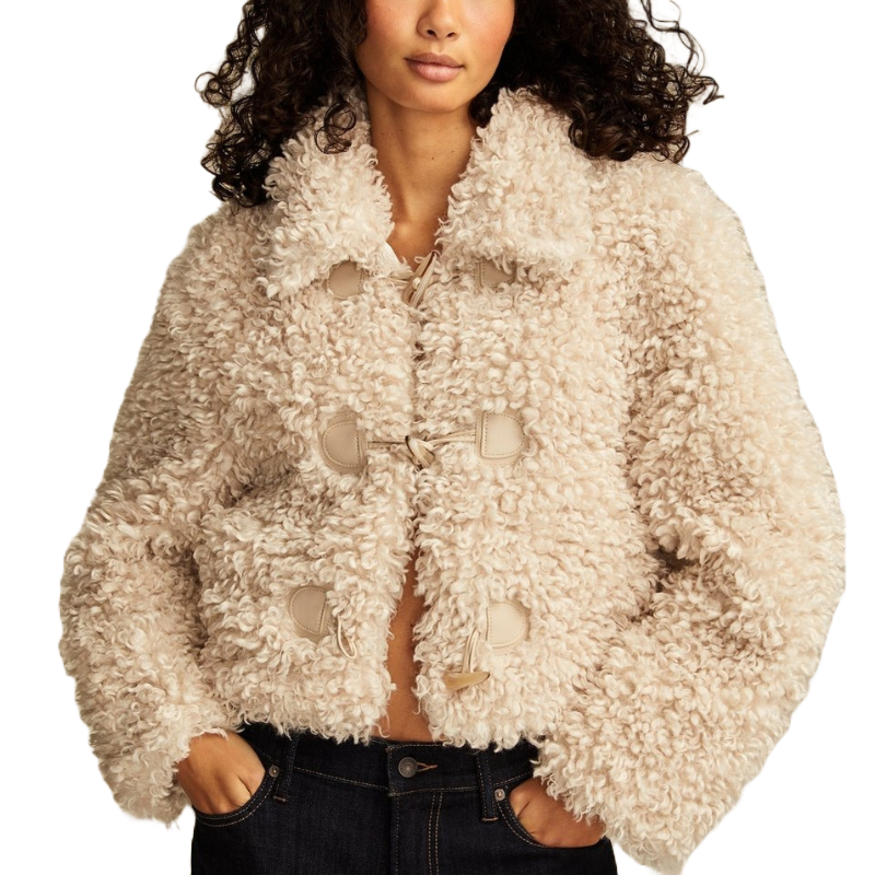 A short, cream-colored faux teddy jacket with a toggle-style closure and a plush, curly texture. It features a collar and long sleeves, paired with dark jeans.