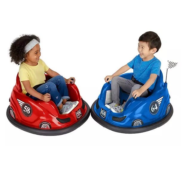 Two children smiling and riding in red and blue toy bumper cars.