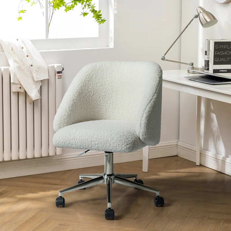 A modern white upholstered office chair with a curved backrest and chrome base on casters, placed near a white desk with a lamp, books, and a laptop.
