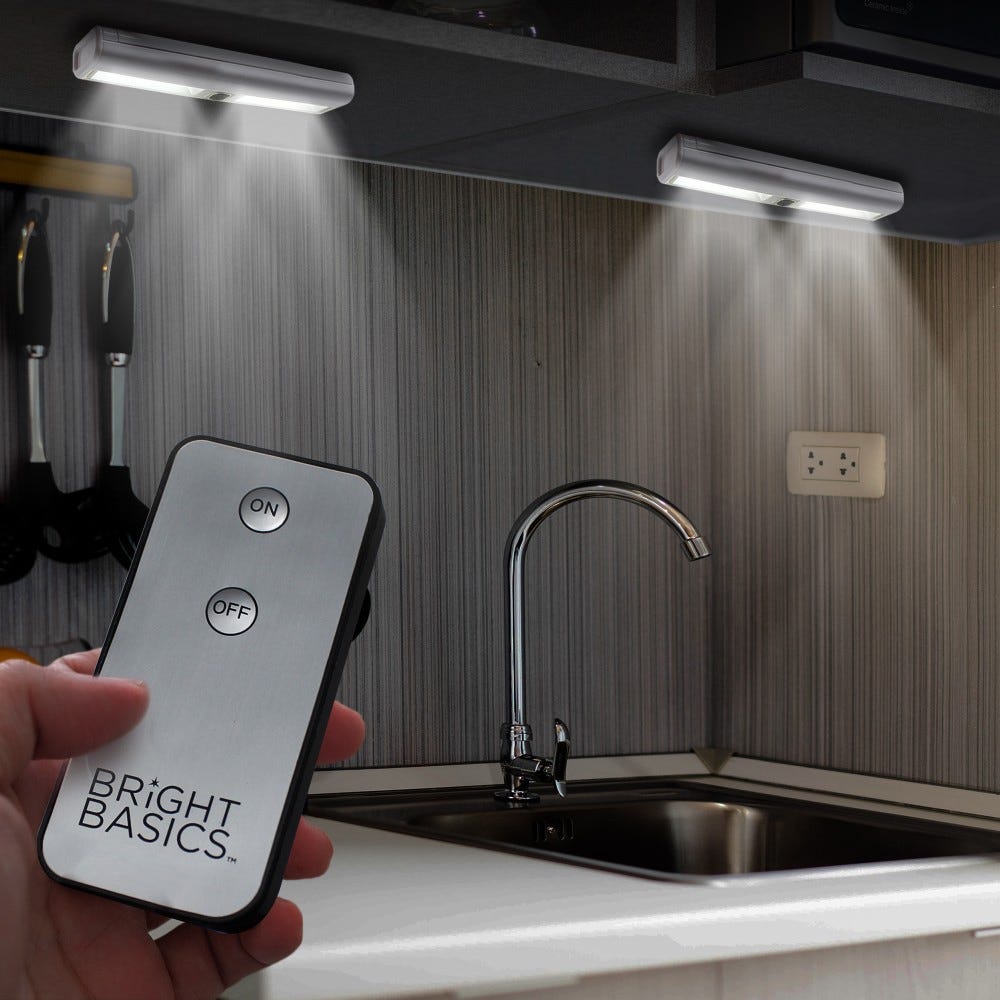 Under-cabinet LED lights are shown being controlled by a remote labeled \“Bright Basics,\“ providing illumination for the kitchen sink area.