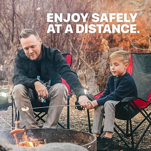 A man and a boy use telescopic s'mores sticks to roast marshmallows over a campfire from a safe distance.