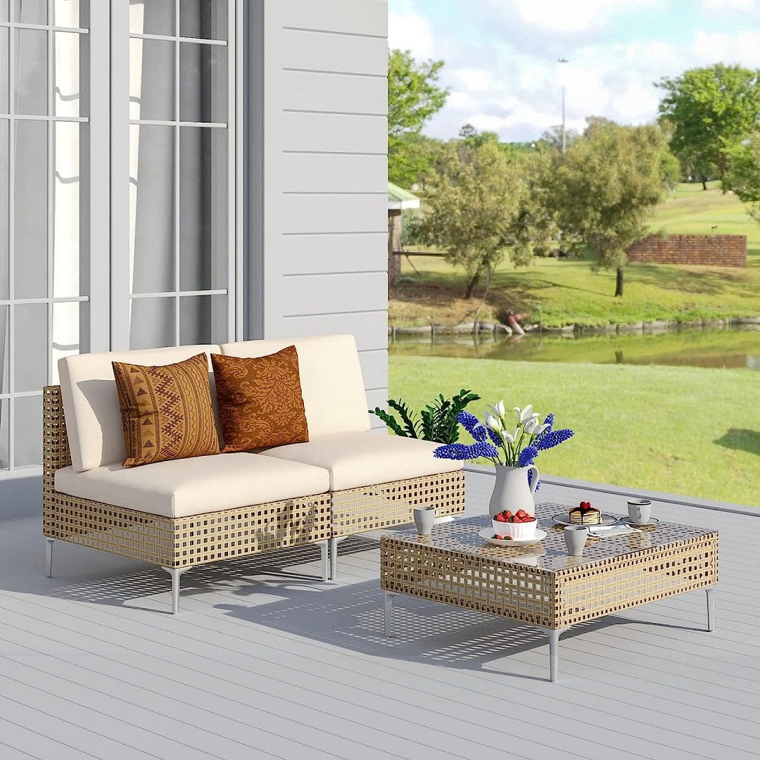 Outdoor wicker patio set with a two-seater sofa and a matching coffee table, both with beige cushions, set on a porch overlooking a yard.