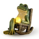 A statue of a frog sitting on a rocking chair with a solar-powered light resembling a candle on its lap.